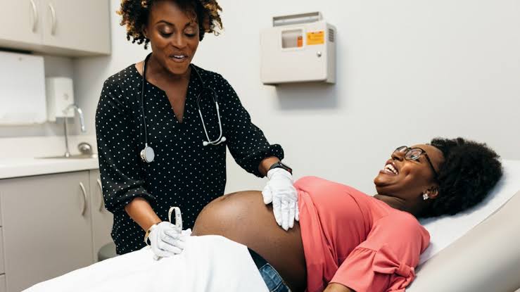 Midwife examining a smiling pregnant woman during an antenatal visit